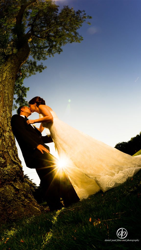 Outdoor photo of a bride and groom at sunset with the sun shining through between the couple.