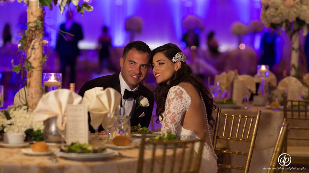 Photo of a bride and groom smiling at a table at their reception.