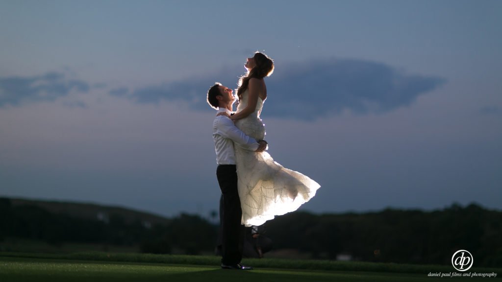 A groom lifting his bride outdoors.
