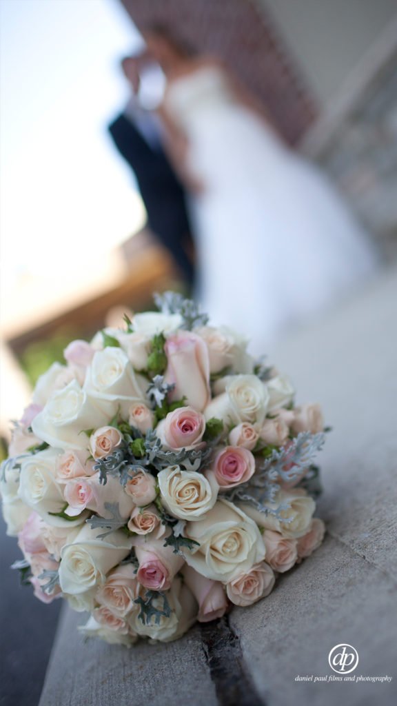 Cinematic shot of a bouquet of flowers in the foreground and a bride and groom standing behind them out of focus.